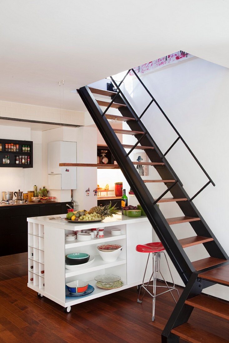 Kitchen with staircase in front of kitchen island on casters with crockery in shelving