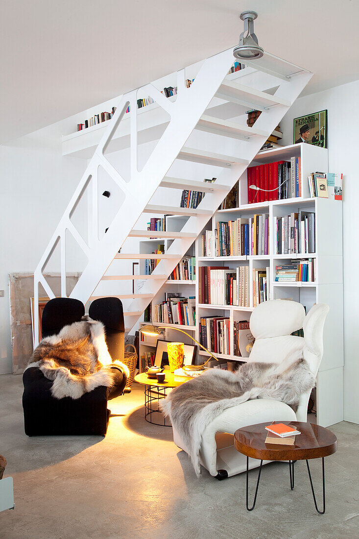 Reading corner with two armchairs and bookshelf under a white staircase