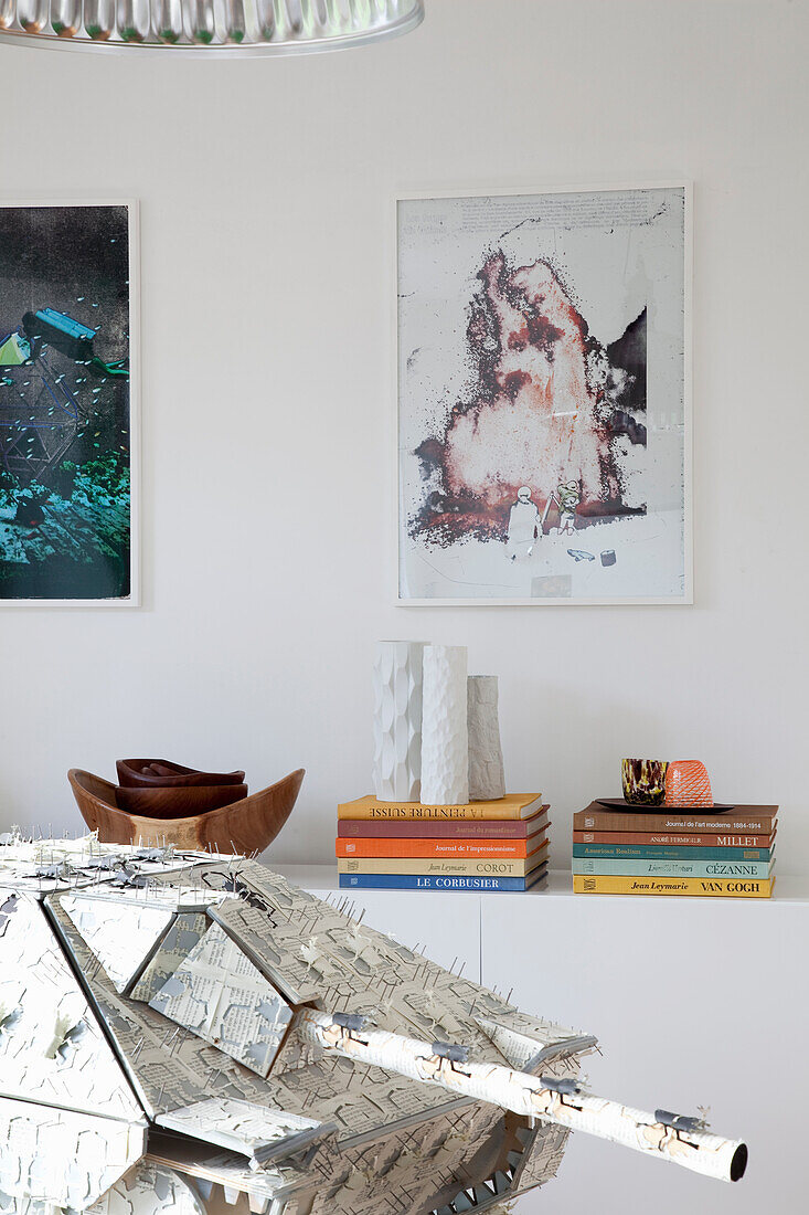 Armour model and stack of books in front of a white wall with artwork