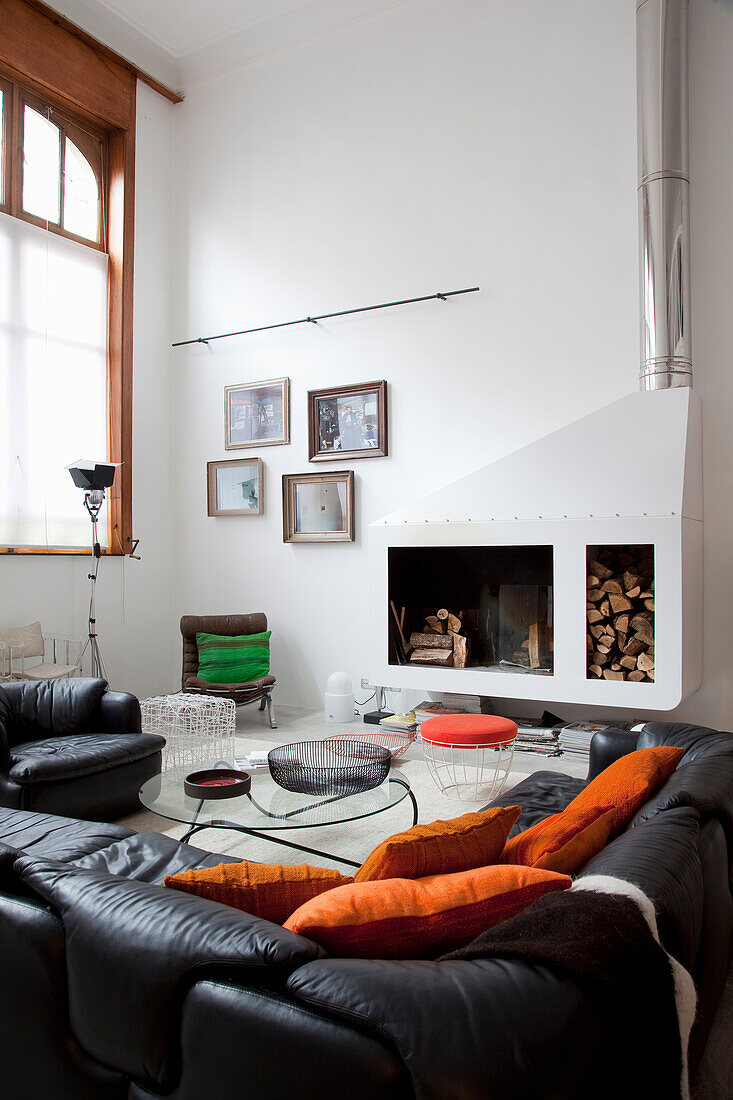 Living room with fireplace, black leather sofas and orange-coloured cushions