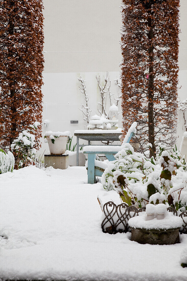 Snow-covered garden area with bench and planters in winter