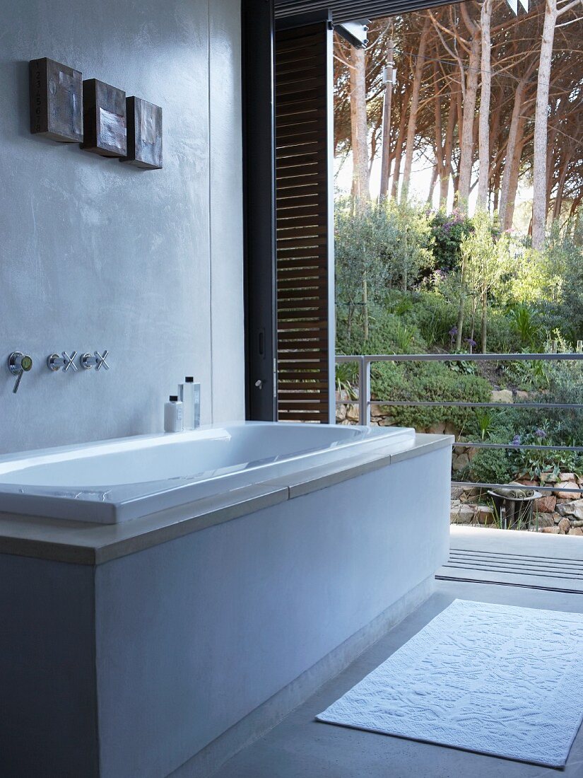 Modern bathtub in front of open terrace door with view of tropical garden