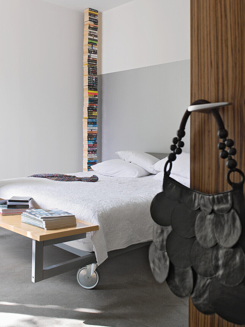 Minimalistisches Schlafzimmer mit Bücherstapel als Dekosäule und Bett mit Rollen