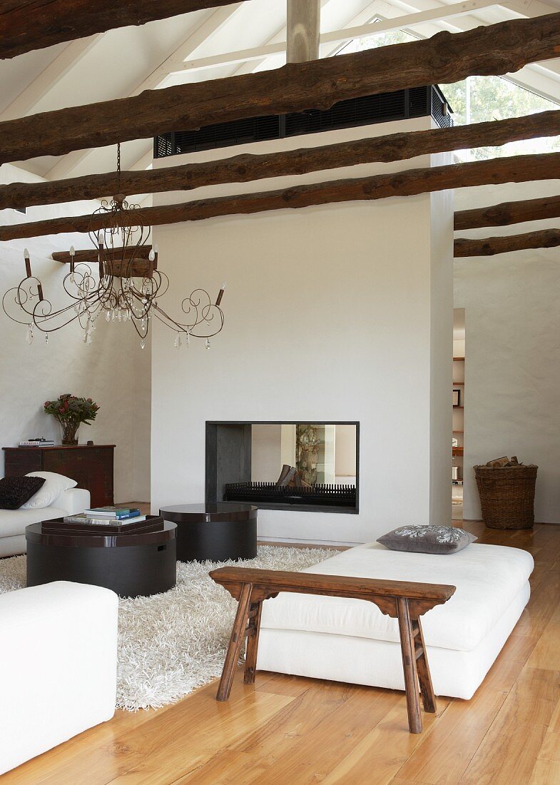 Offener Kamin als freistehender Raumteiler im offenen, modernen Wohnraum mit rustikalen Baumstämmen als Dachbalken