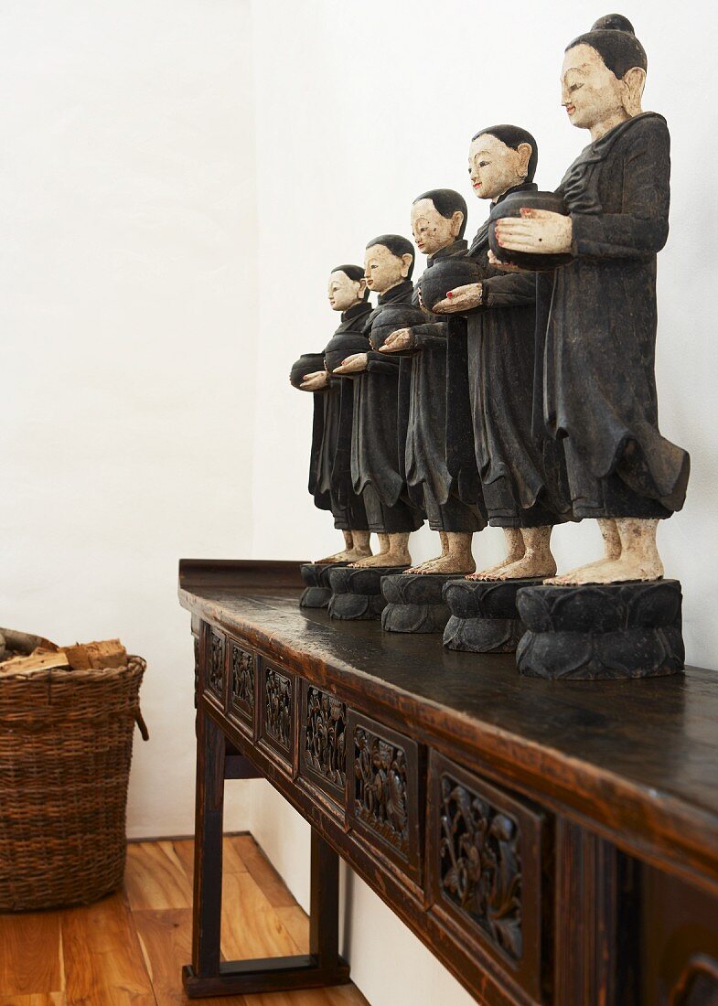 Schwarzgekleidete Mönchsfiguren auf exotischem Konsolentisch und Korb mit Brennholz