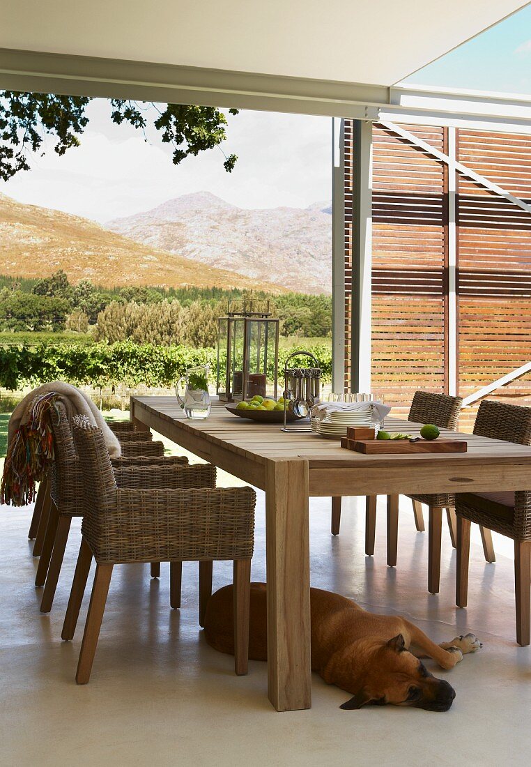 Wooden chairs with wicker seats and hand-crafted, modern wooden table on roofed terrace with amazing view of landscape