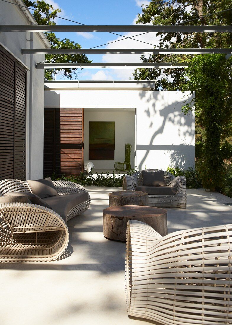 Licht- und Schattenspiel auf moderner Terrasse mit ausladenden aber filigran gearbeiteten Loungemöbeln und Tischen aus alten Stämmen tropischer Bäume