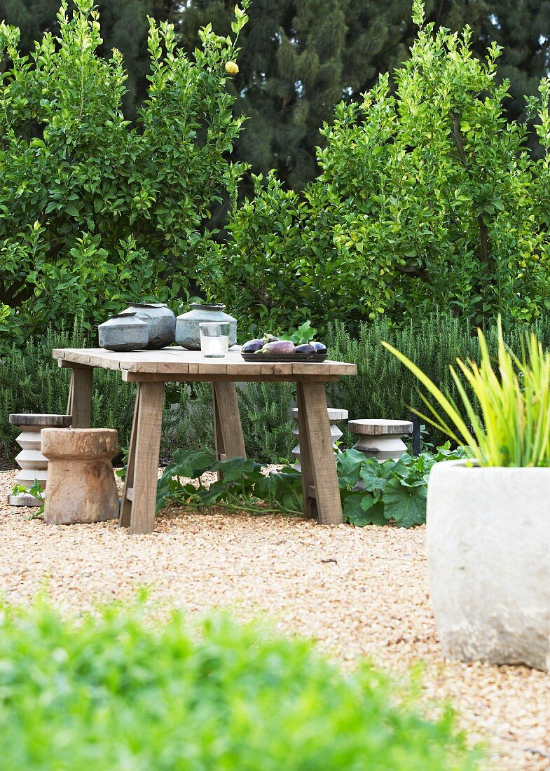 Rustikaler Tisch mit vier Hockern auf Kiesfläche im Garten