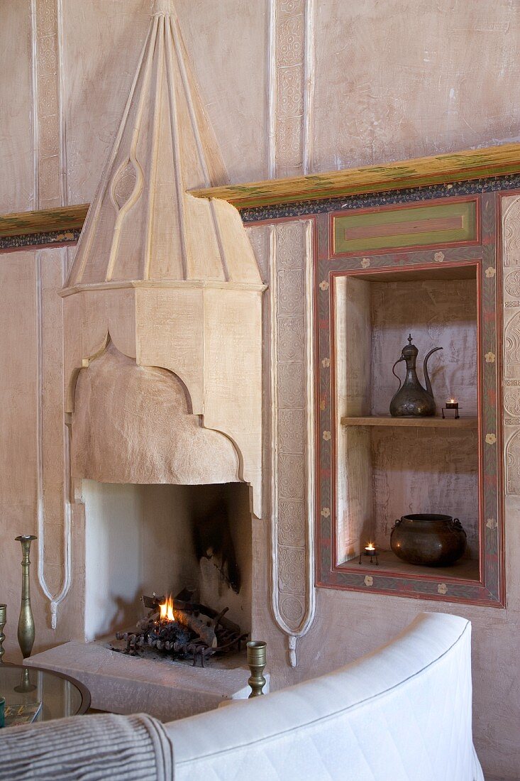 Open fireplace with Oriental elements, ornate copper vessels in niche and collection of candlesticks