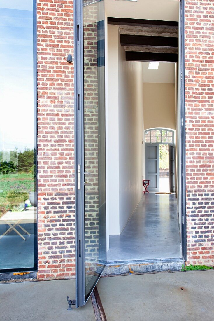 View through open glass door through long hallway to open front door at other side of brick building