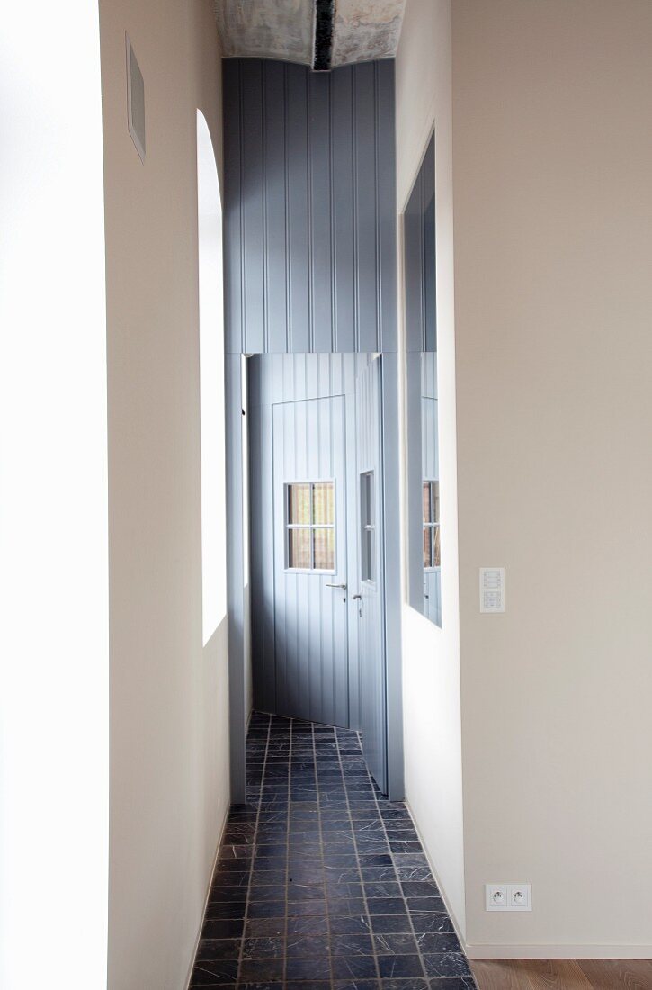 Narrow corridor with tiled floor and mirror opposite window