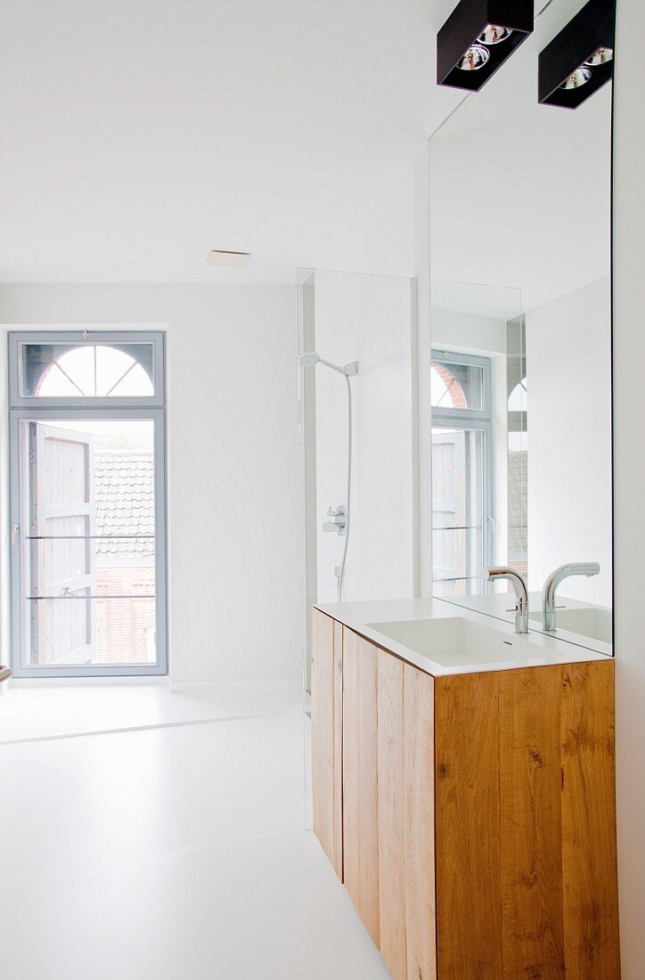Modern, white bathroom with arched window and washstand below large mirror