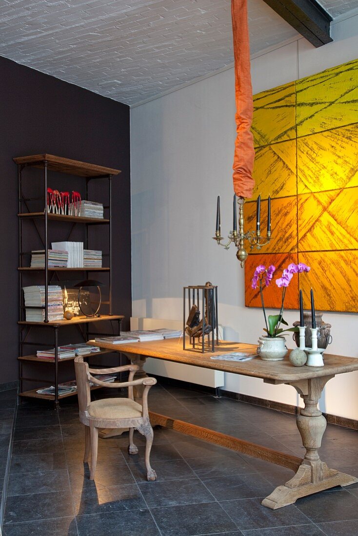 Stilmix in Raum mit Loftcharakter - rustikaler, alter Holztisch mit Dekoration und antiker Armlehnstuhl vor moderner Kunst in Gelbtönen