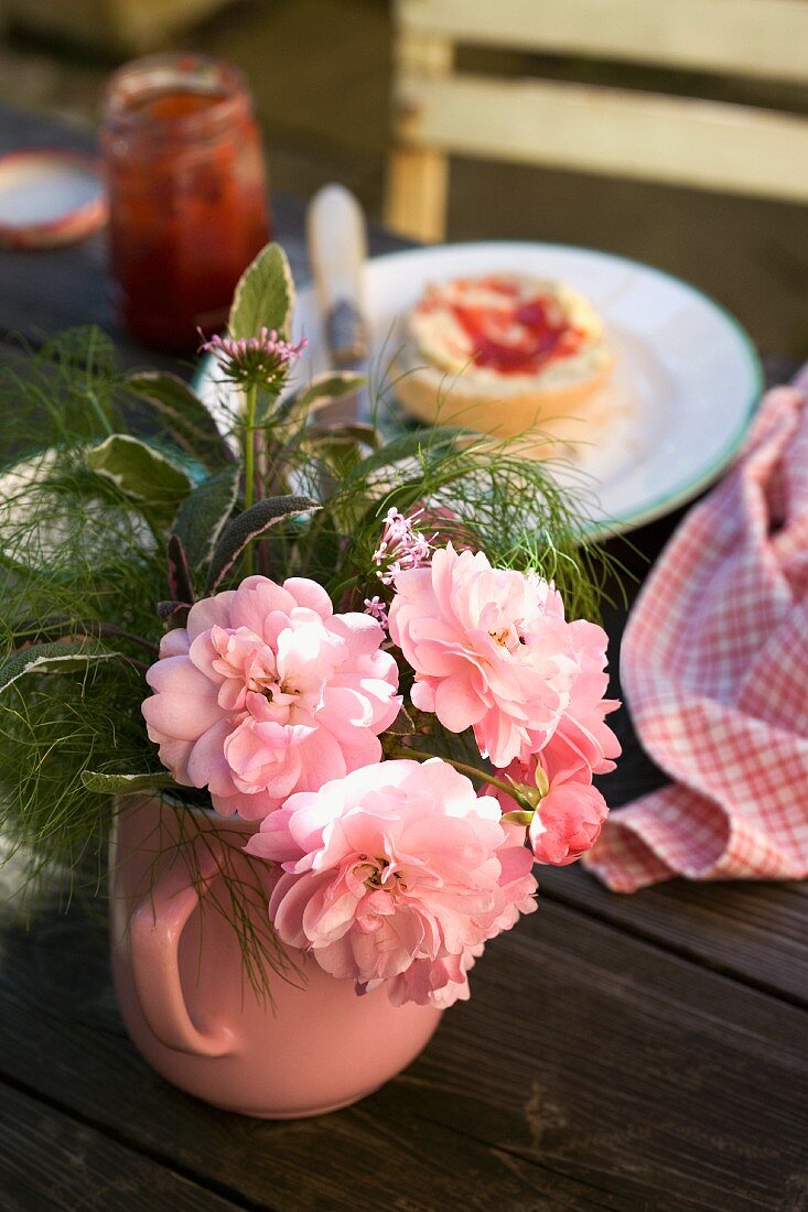 Kleiner Gartenstrauss mit Rosen in rosa Kännchen auf Frühstückstisch
