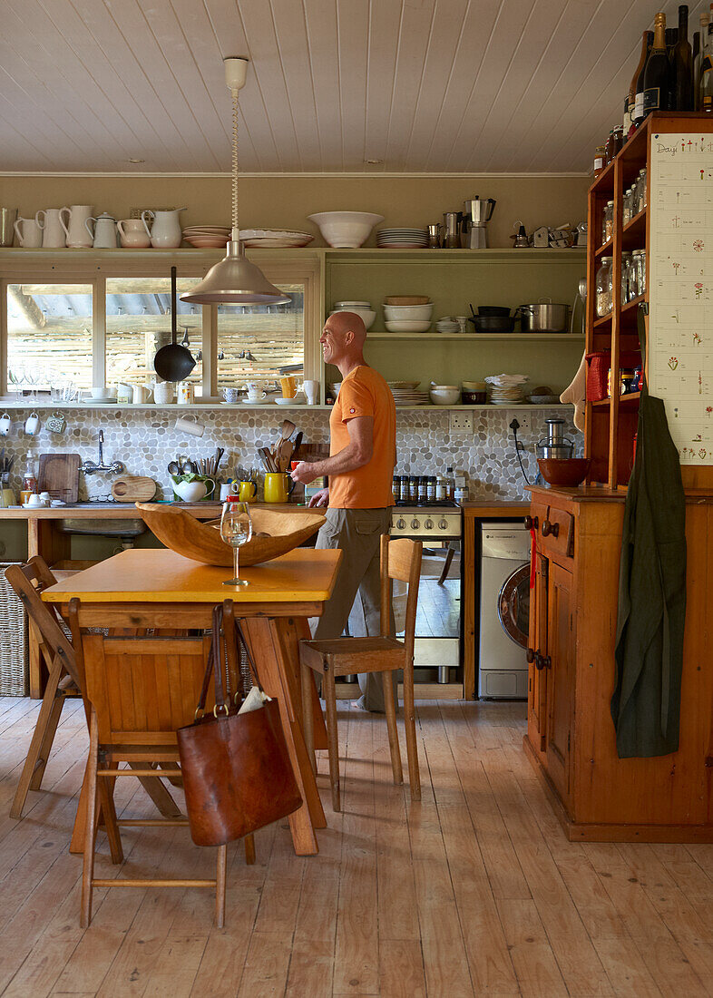 Man in kitchen with dining table, wooden furniture and shelves