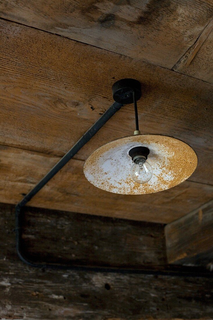 Vintage pendant lamp with rusty lampshade hanging from wooden ceiling