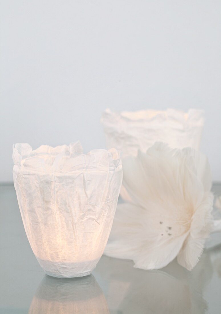 Kunstvolle Windlichter aus Seidenpapier, Kleister und Klarsichtfolie, daneben eine duftige, weiße Blüte