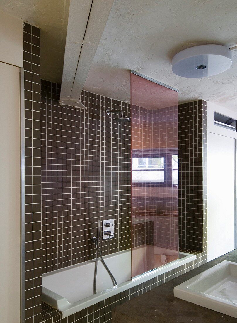 Bathtub in niche with brown mosaic wall tiles