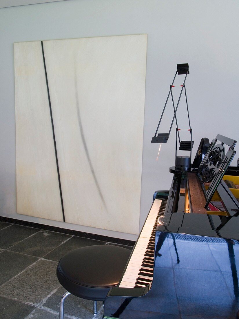 Hocker mit schwarzem Lederbezug und Klavierflügel vor modernem Bild an Wand