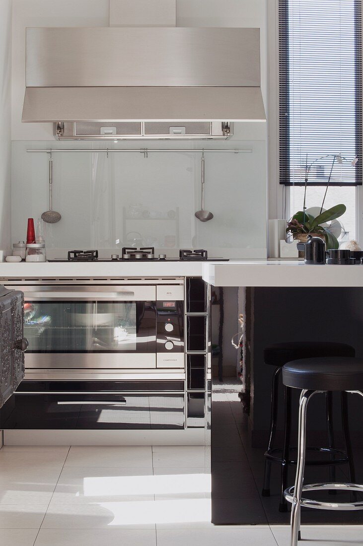 Sonnenflecken in der modernen, Schwarzweißen Küche aus spiegelnden Materialien und Barhocker an der Küchentheke