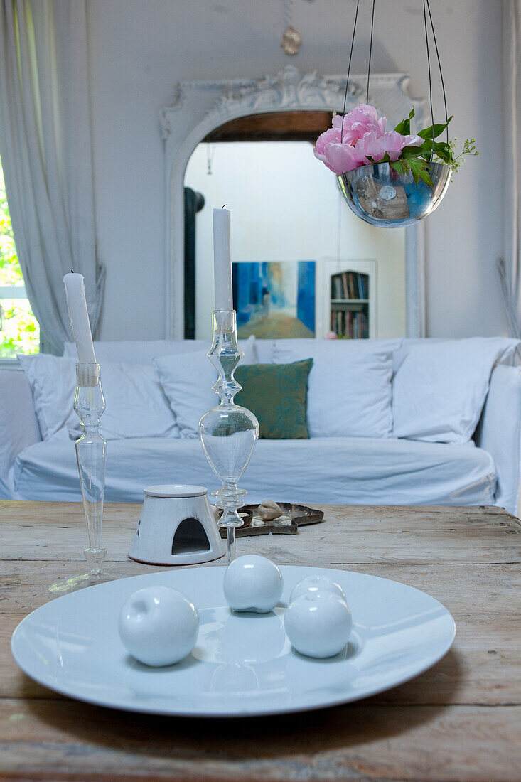 Living room with white sofa, rustic wooden table, candle holder, porcelain decor and DIY hanging basket with peony