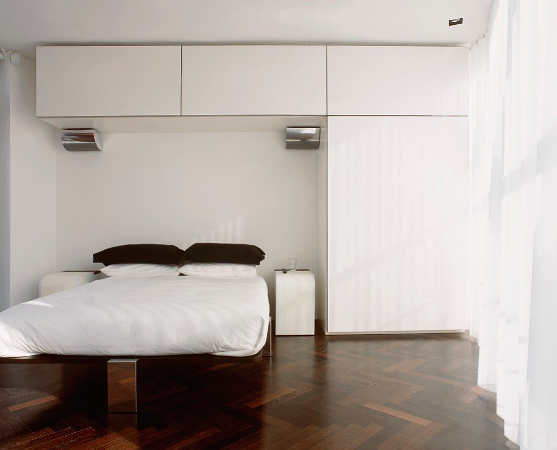 Designer bedroom with white fitted wardrobe and dark parquet floor