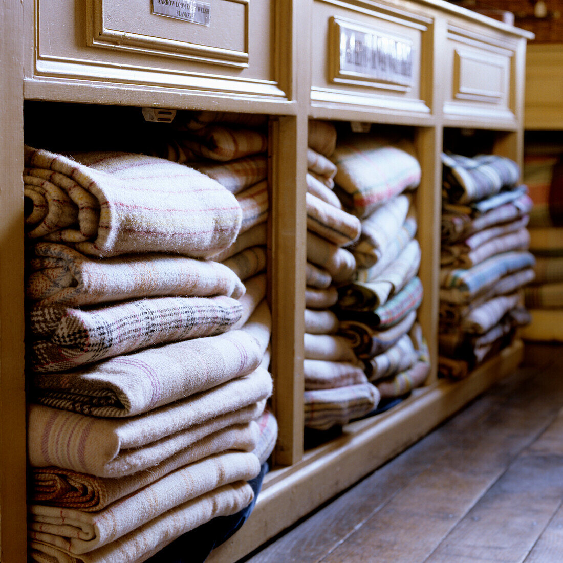 Folded blankets in various patterns on a wooden shelf