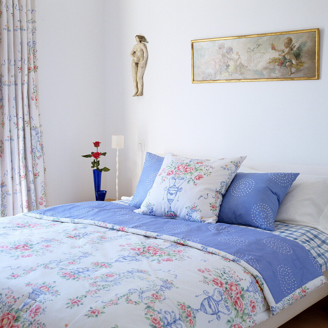 Bed with floral bed linen, picture and figurine on the wall