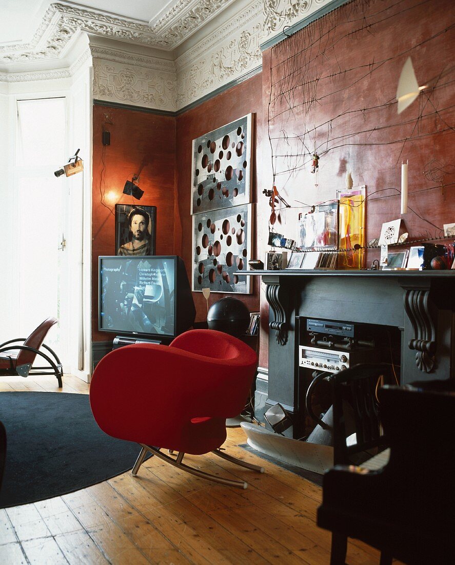 Roter Designersessel vor Kamin mit eingebauter Stereoanlage im luxuriösem Wohnraum im Barockstil