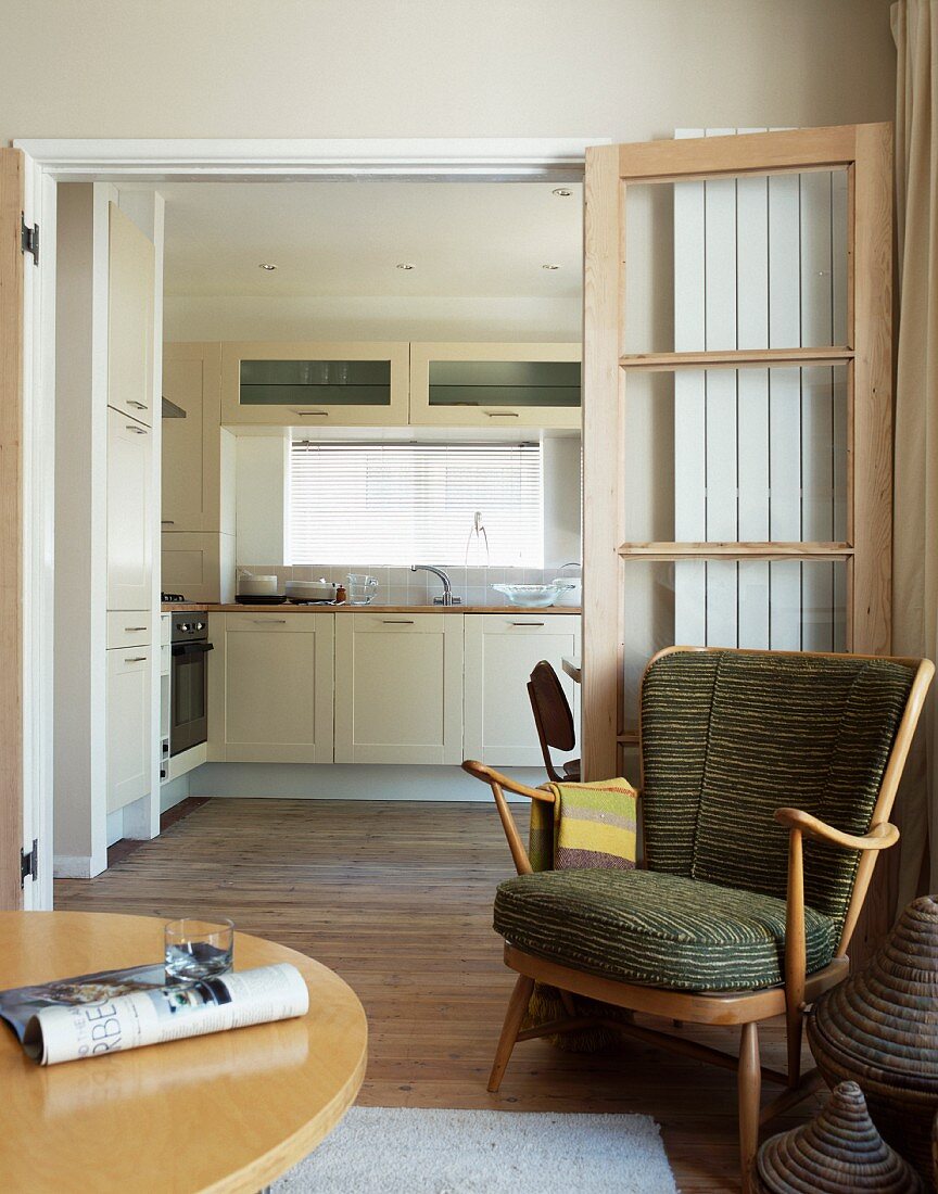 Sessel im 50er Jahre Stil vor offener Flügeltür mit Blick in moderne Küche