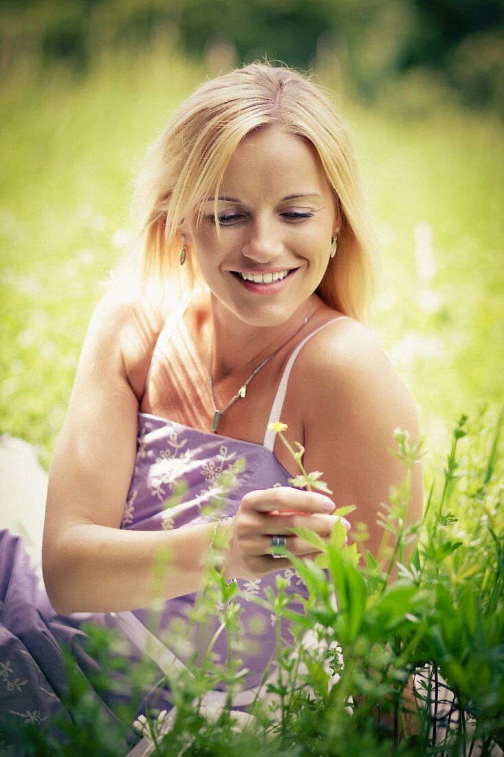 Junge blonde Frau sitzt auf einer Blumenwiese