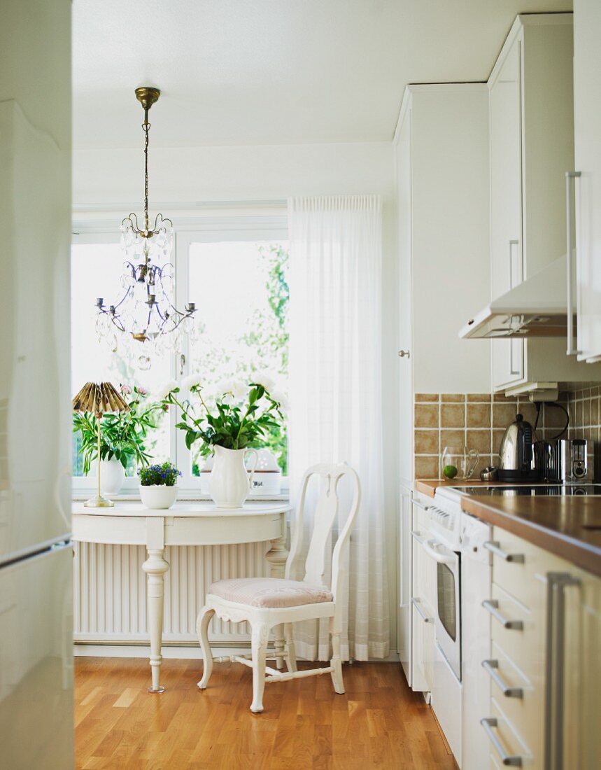 Ein antiker Wandtisch und Stuhl in Weiß vor dem Fenster verleihen der modernen Küche einen romantischen Vintagetouch