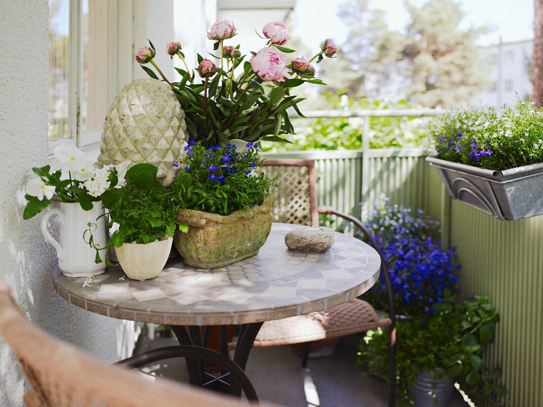 Mosaiktisch und Rattanstühle auf dem Balkon mit viel Blumendeko in verschiedenen Gefäßen