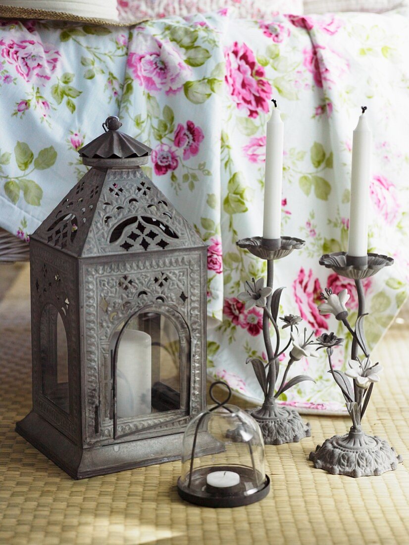 Oriental lantern and candlesticks in front of floral bedspread