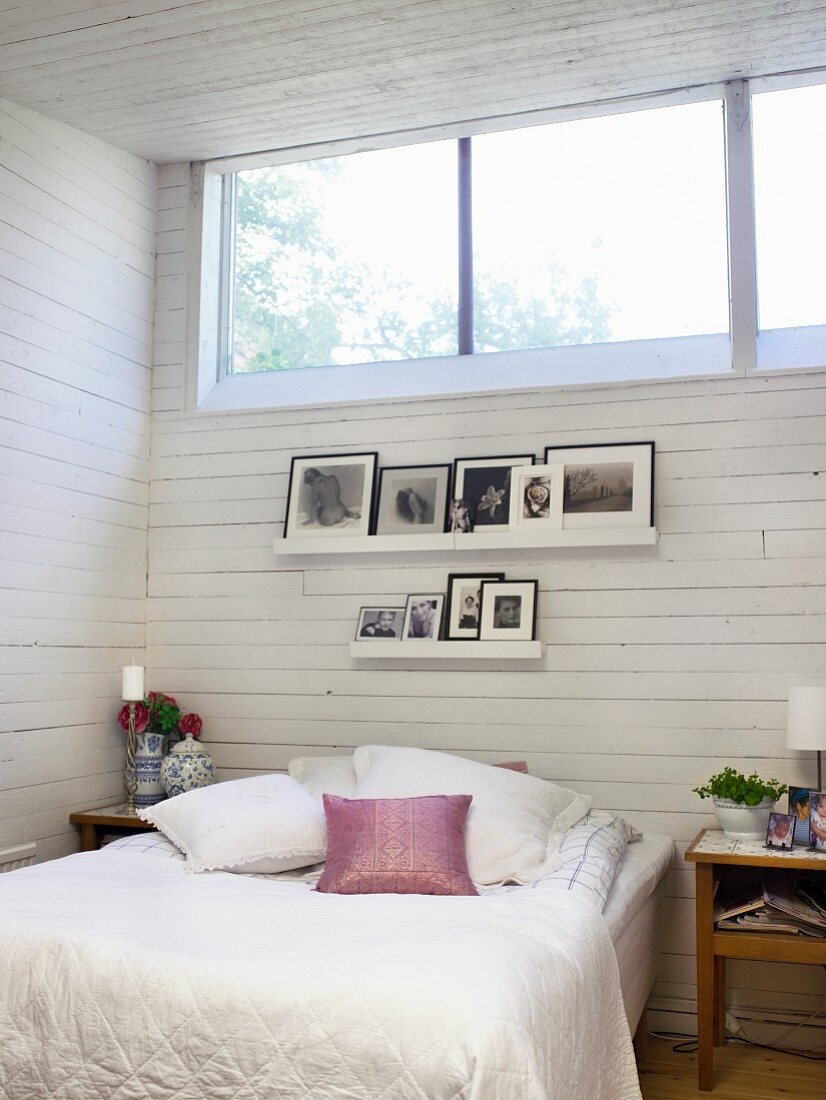 Weisses Schlafzimmer mit eingerahmten Fotos über dem Bett