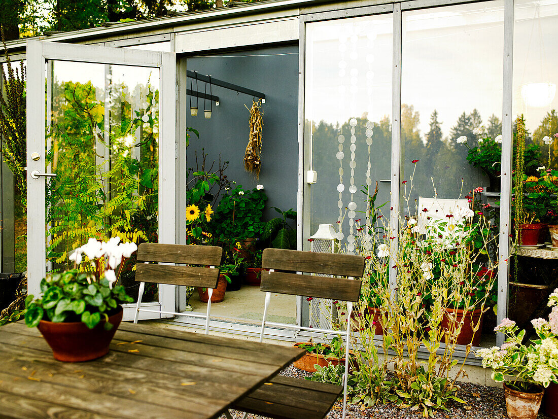 Terrasse mit Holzmöbeln und Pflanzen vor einem Wintergarten