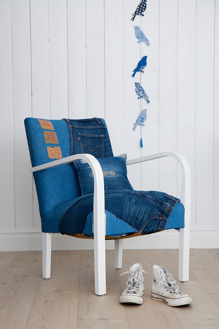Stuhl mit Jeansbezug und Vögel-Wanddeko, weiße Sneaker davor auf Holzboden