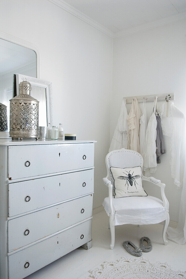 Weißes Schlafzimmerinterieur mit dekorierter Kommode und Stuhl