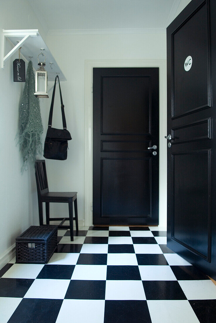 Flur mit schwarz-weiß kariertem Boden und schwarzer Tür mit WC-Schild