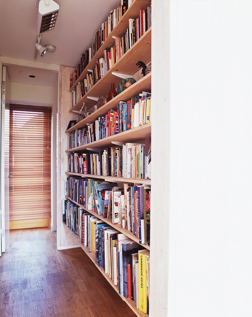 Raumhohes Bücherregal neben offener Tür mit Blick auf Glastür und Jalousie