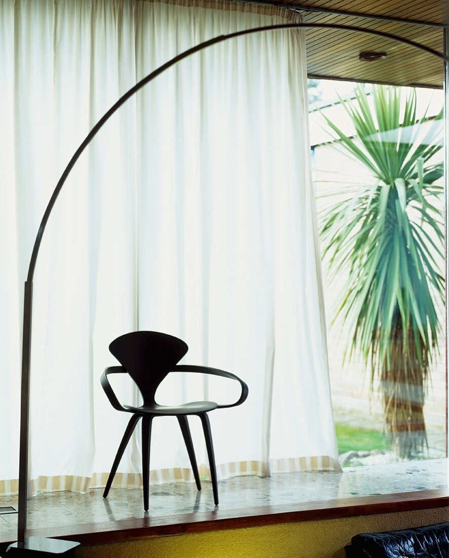 Fifties-style wooden chair in front of half-closed curtain at window and view of yucca