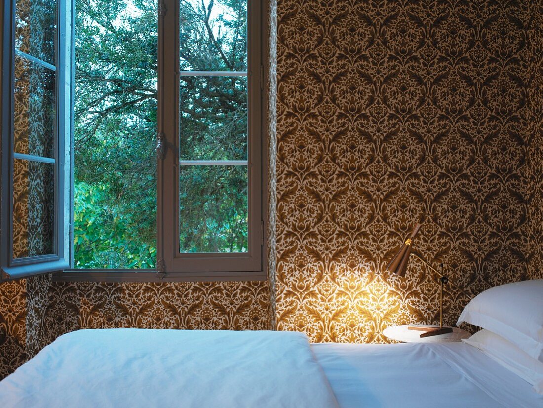 Schlafzimmer mit gold weißem Ornamentmuster auf Tapete an Wand und göffnetem Fenster