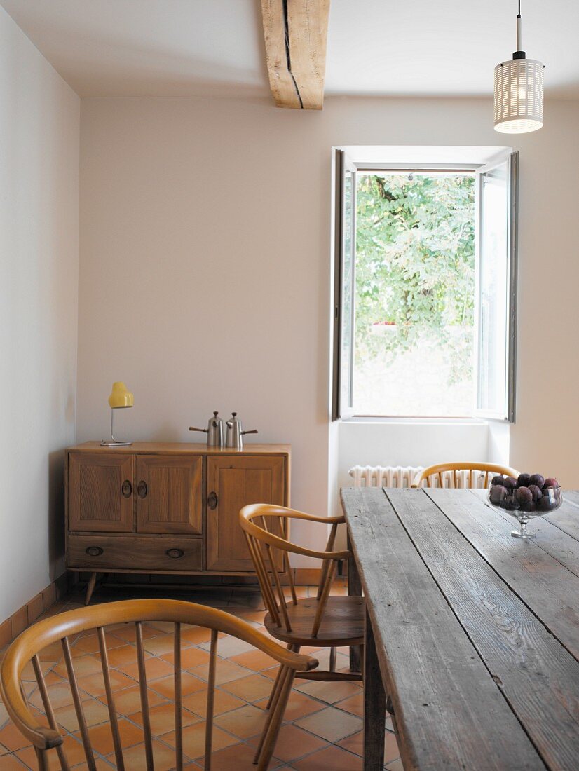 Rustikaler Tisch und Holzstühle vor offenem Fenster im Esszimmer