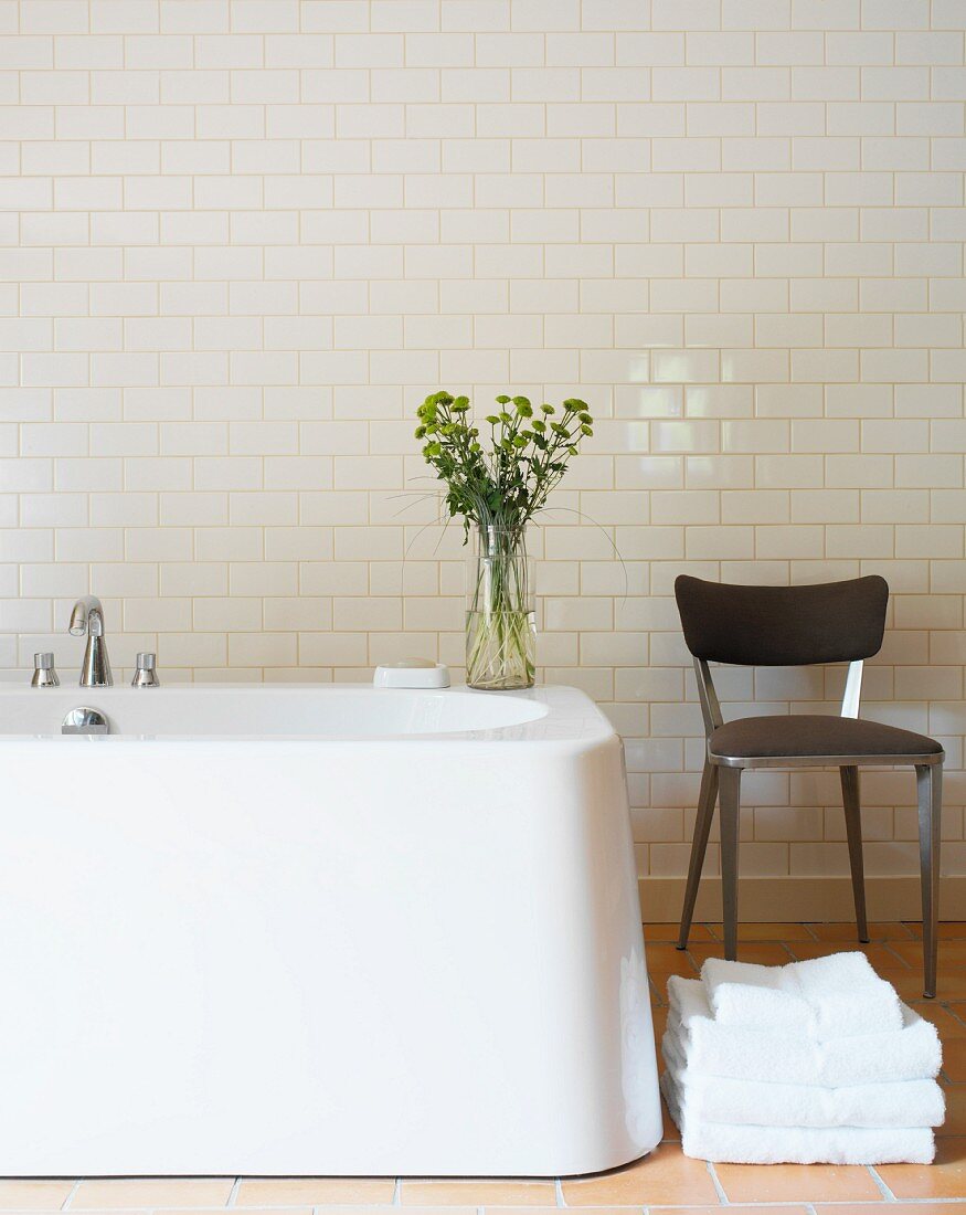 Stuhl neben freistehender Badewanne vor Wand mit weissen Fliesen