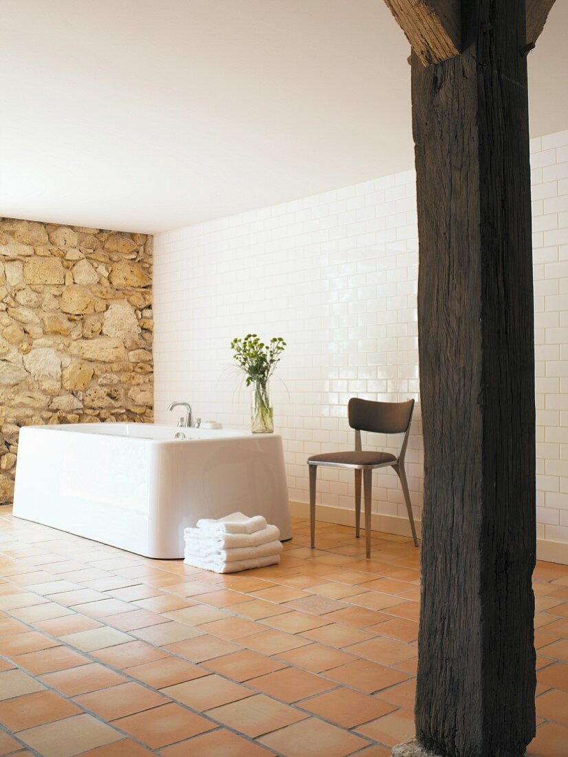 Rustic wooden column in modernised bathroom with free-standing bathtub