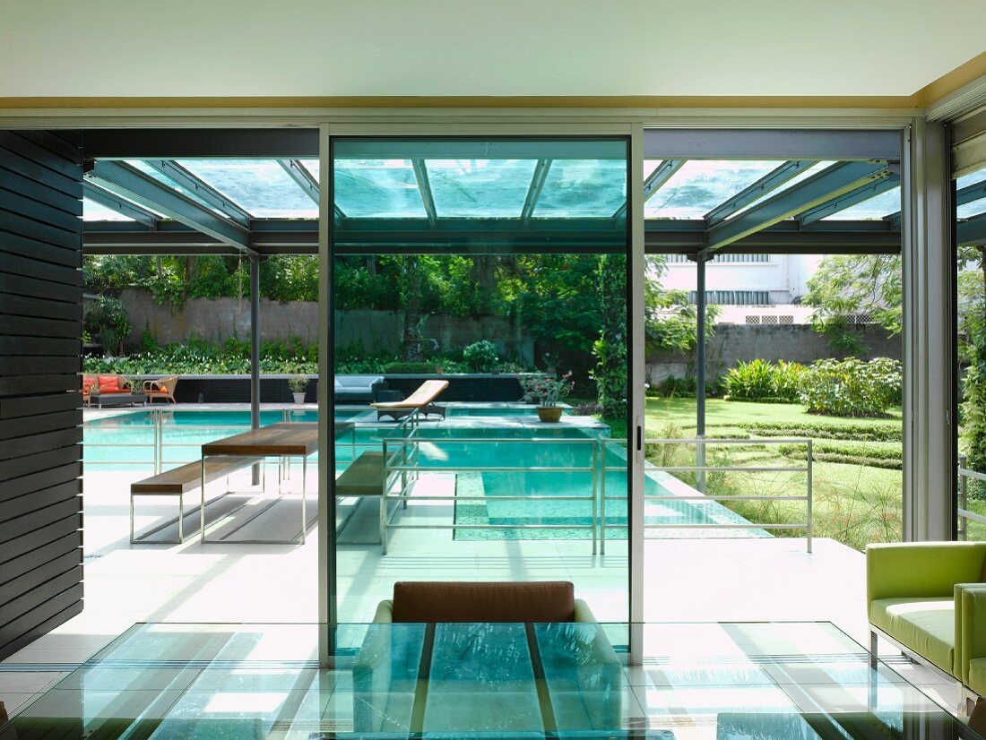 Blick vom Esszimmer mit Glastisch auf überdachte Terrasse mit Pool