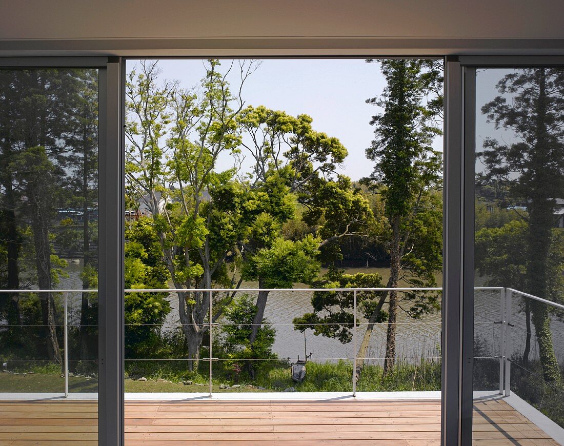 Open sliding doors to wooden terrace with intricate metal balustrade and view of trees and lake
