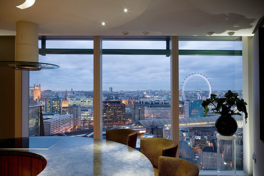 Round kitchen counter with integrated hob in front of large windows with a view of London