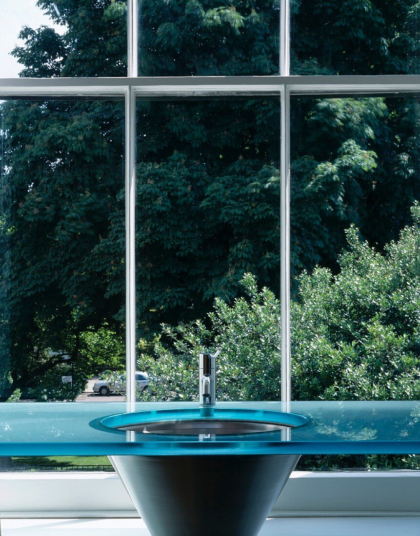 Designer Waschbecken mit blauer Glasplatte vor Sprossenfenster mit Blick auf Bäume