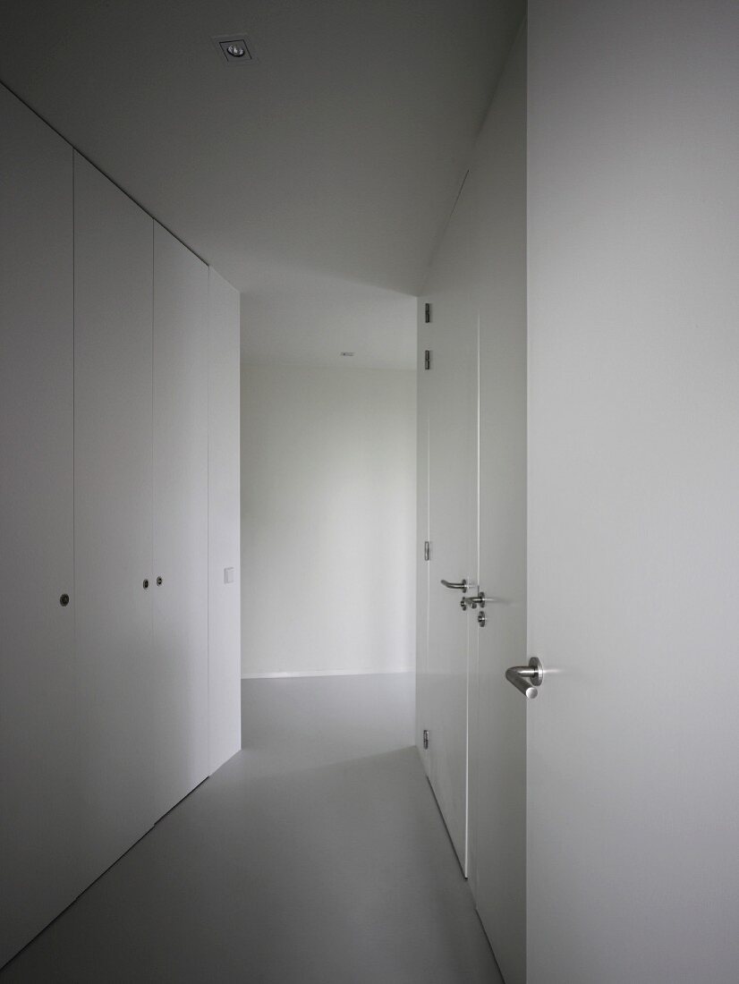 Corridor with smooth-fronted fitted cupboards and stainless steel handles on integrated doors flush with wood cladding